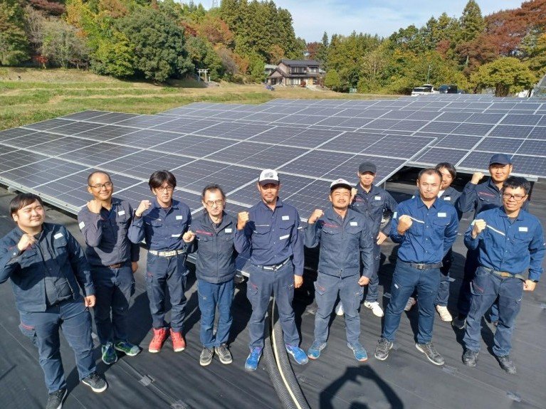 メガソーラー発電所の建設現場でガッツポーズをする施工チームと広大な太陽光パネル