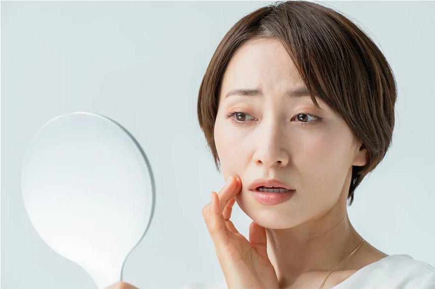 鏡を見てほうれい線や口元のたるみを気にする中高年女性