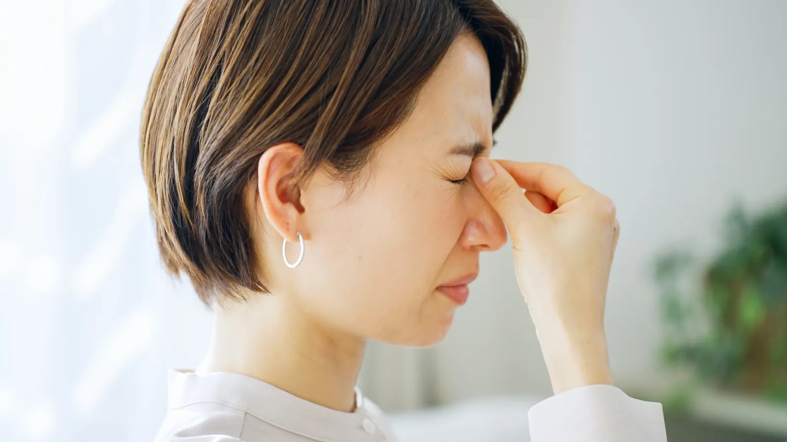 長時間のデスクワークやスマホ使用で目の疲れ（眼精疲労）を感じ、目頭を押さえる女性のイメージ