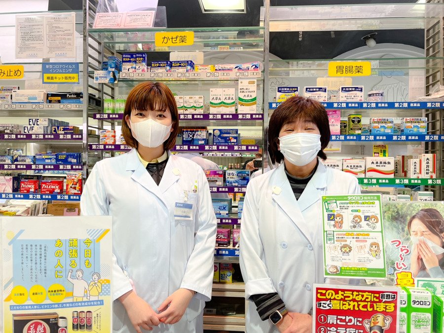 日本のドラッグストア店内でかぜ薬や胃肠薬の棚の前に立つ2名の女性薬剤師