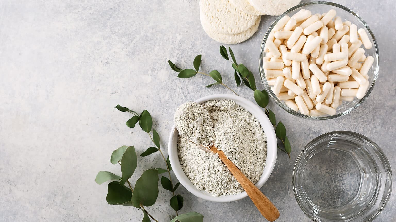 テーブルに置かれたコラーゲンパウダーとカプセルサプリメント、水、ユーカリの葉。美容と健康のためのコラーゲン摂取イメージ