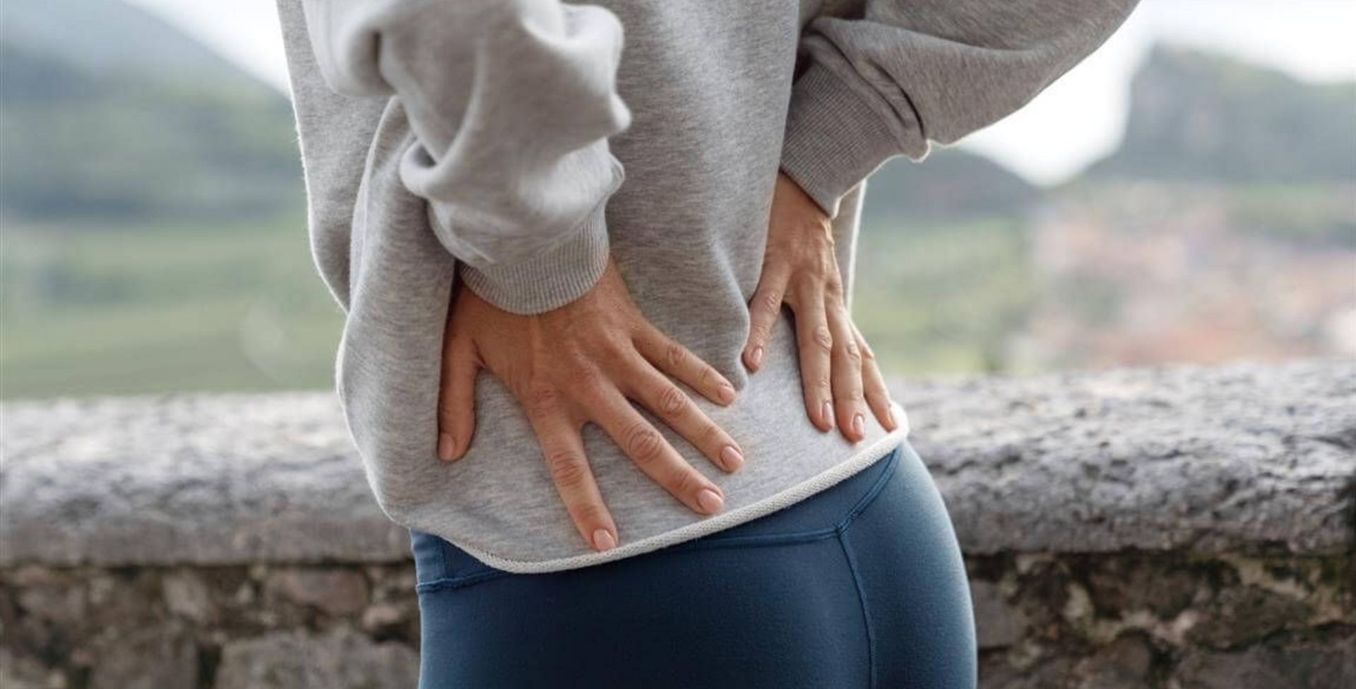 屋外で腰に手を当てて腰痛や背中の痛みを感じている女性の後ろ姿