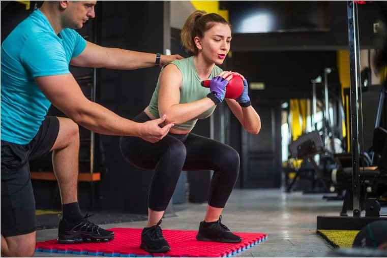 パーソナルジムで専属トレーナーからマンツーマン指導を受けながらスクワットをする女性