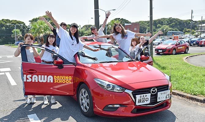 伊沢自動車教習所の赤い教習車と合宿免許を楽しむ女性グループ