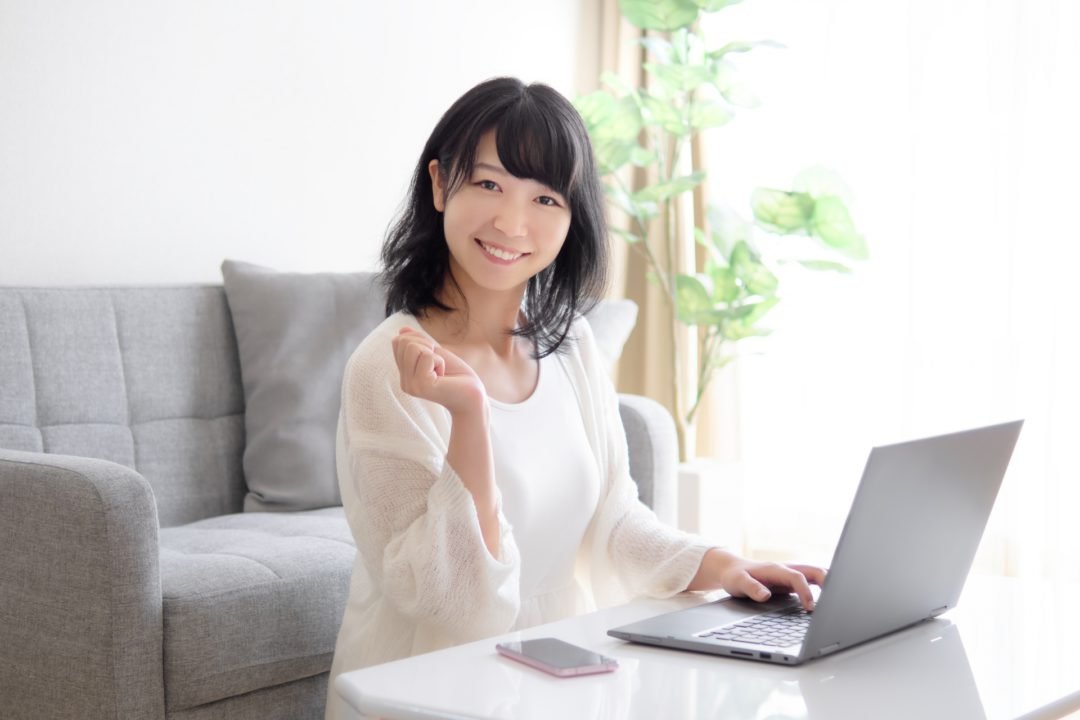 リビングでパソコンを使って在宅ワーク（データ入力・ライティング）をする笑顔の女性