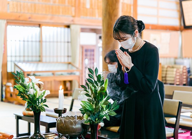 家族葬の葬儀会場で数珠を手に持ち静かに合掌し故人を偲ぶ参列者の様子
